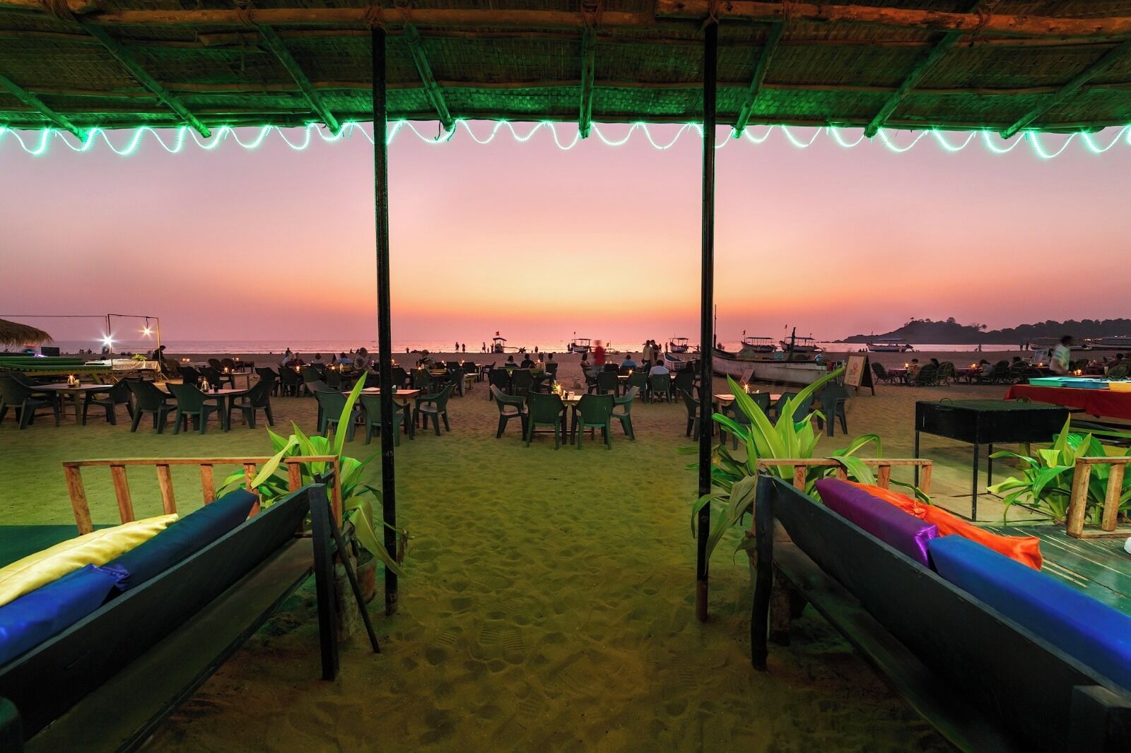 A beachside restaurant with outdoor seating and a view of the ocean at sunset.