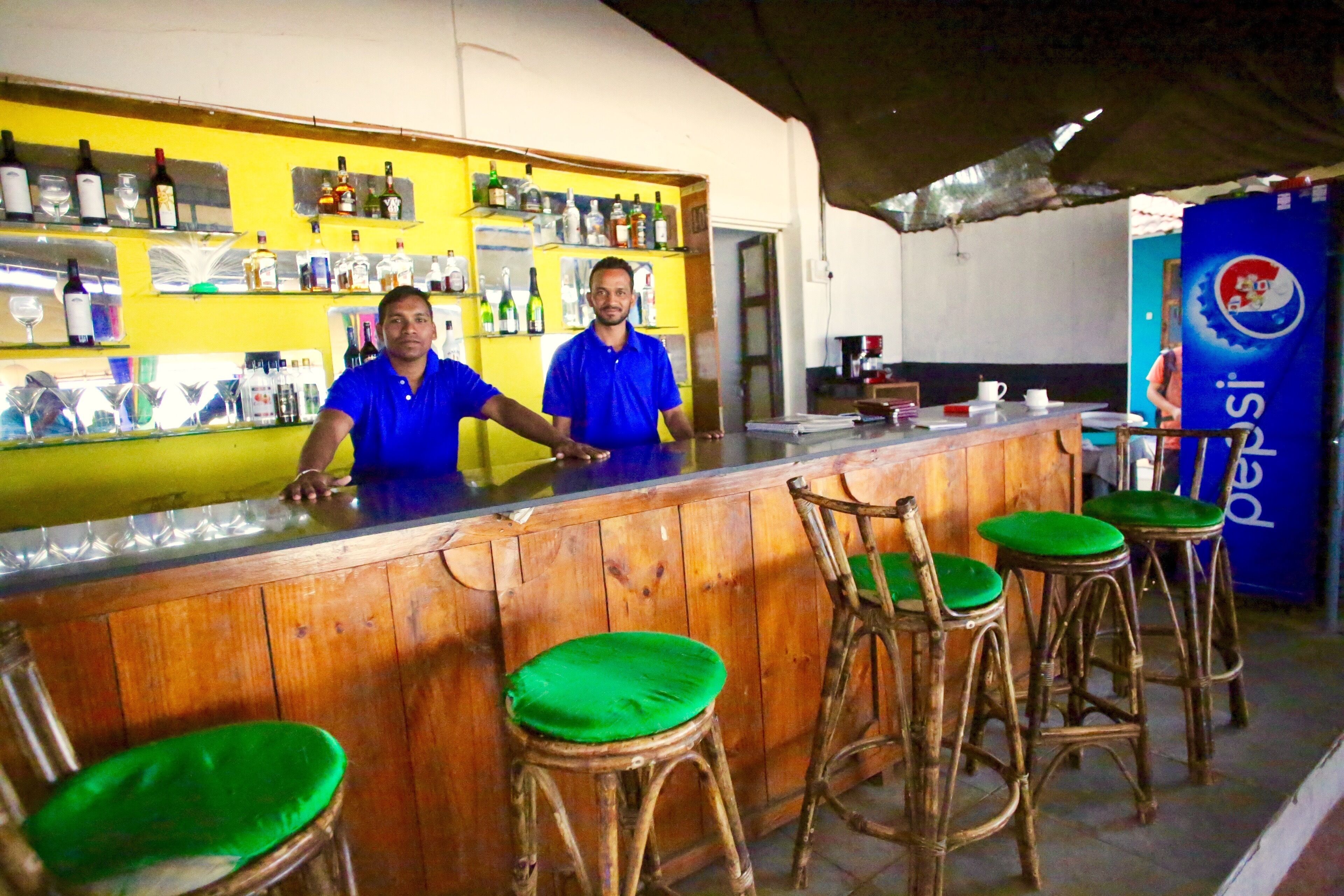 Zona de bar con mostradores de madera y taburetes acolchados verdes.