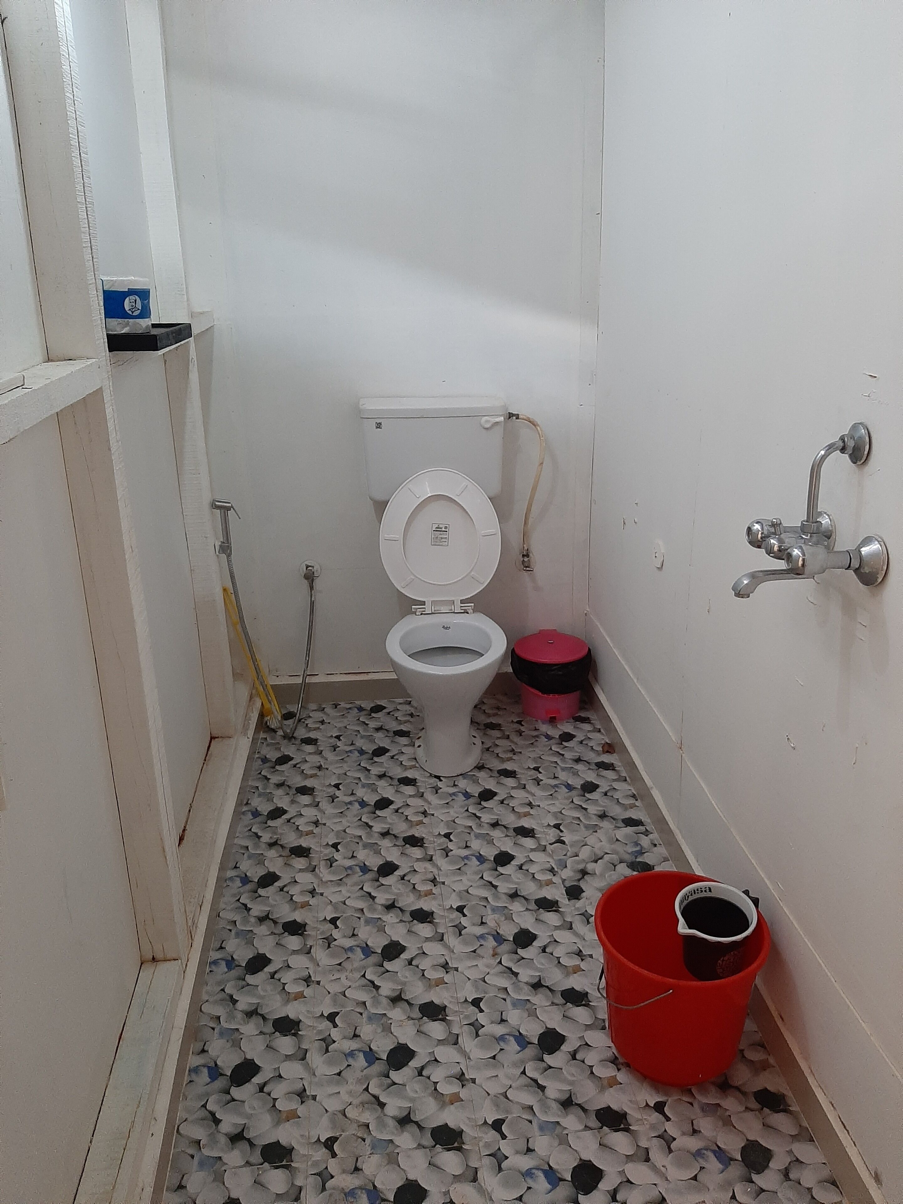 A small bathroom with a toilet, a red bucket, and a shower.
