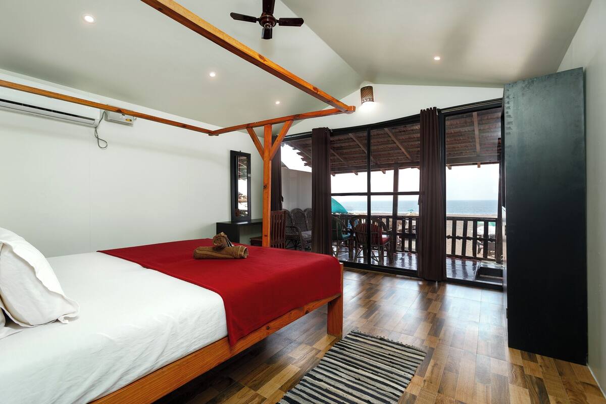 A bedroom with a wooden bed, a red bedspread, a ceiling fan, and a view of the balcony.