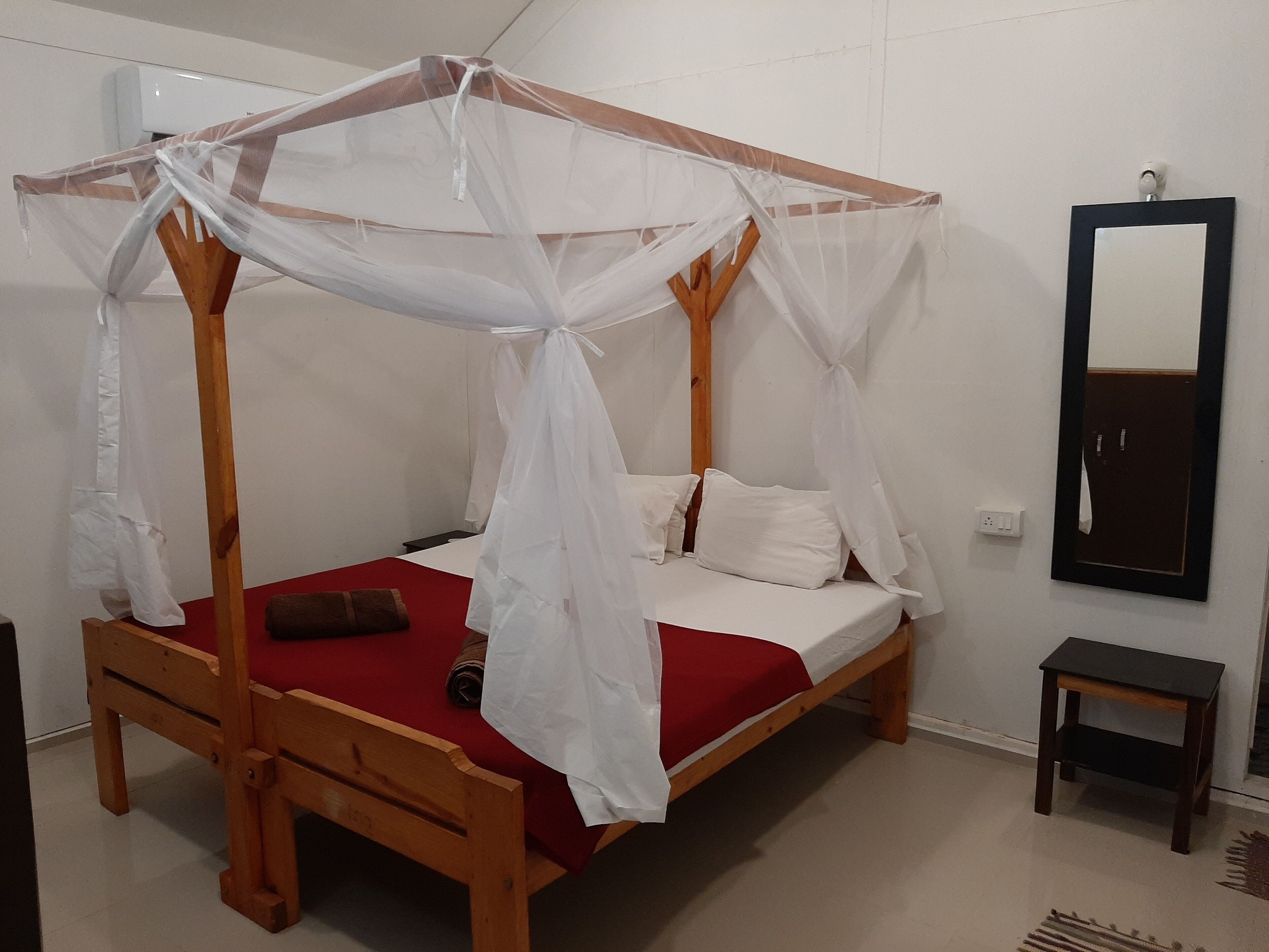 A wooden four-poster bed with a white canopy, a red bedspread, and white pillows. There is a small wooden nightstand beside the bed.