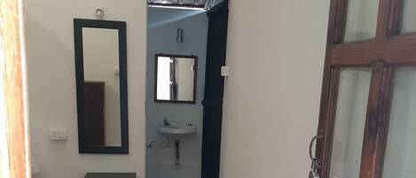 Un pasillo con un banco de madera, un espejo, un lavamanos y una puerta con paneles de vidrio.