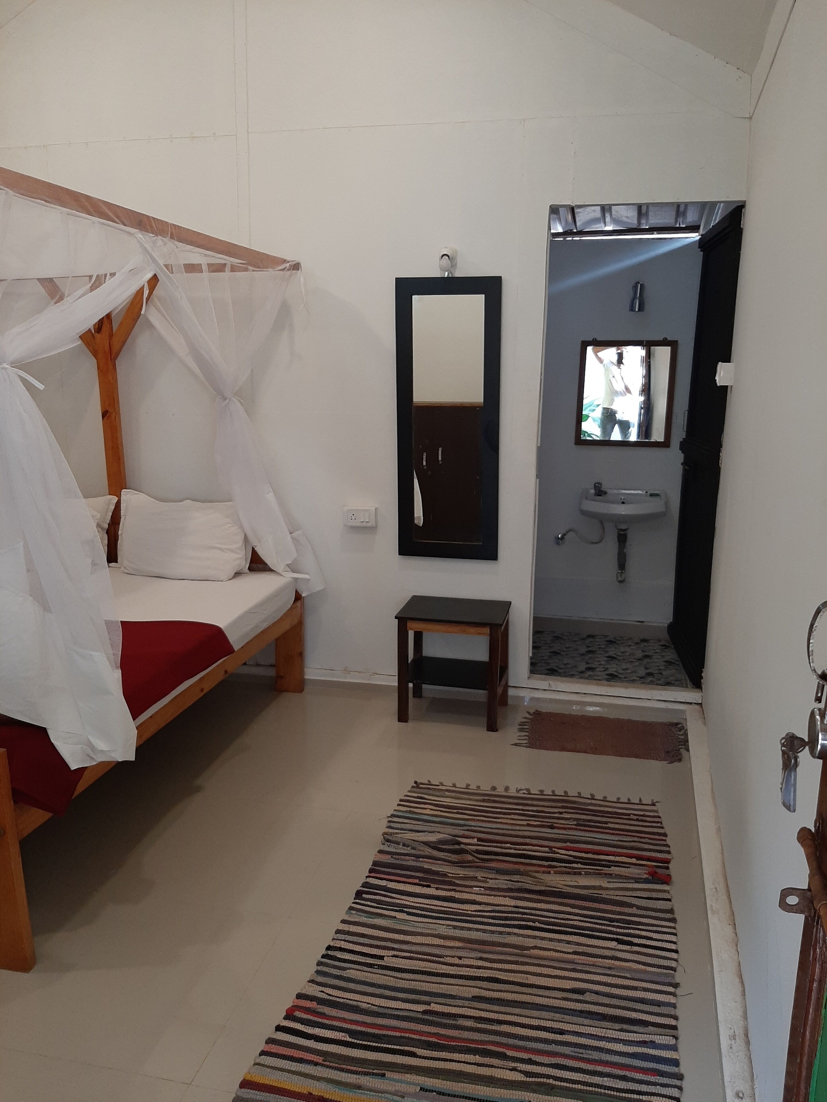 Une chambre à coucher comprenant un lit, une table de chevet, un miroir, un lavabo et une porte donnant sur une autre pièce.