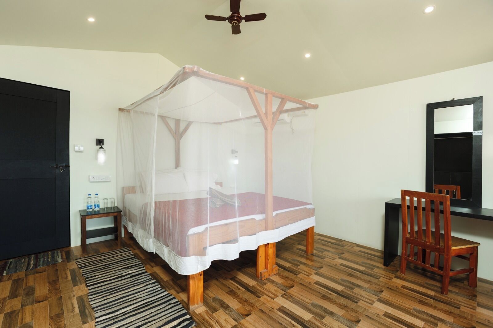 Une pièce avec un plancher en bois, un lit à baldaquin, un bureau avec une chaise, un miroir et une porte.