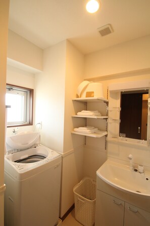 A compact bathroom with a washing machine, a sink, and shelves for toiletries.