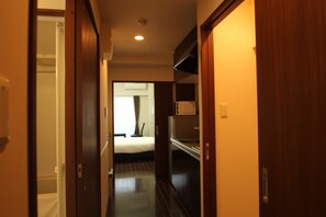 A narrow hallway with wooden doors leading to a bedroom with a bed and a white wall.