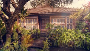 A traditional wooden house with a tiled roof, surrounded by lush greenery and a small pond. - Dragonfly Village (Ubud)