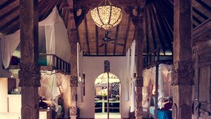An interior with wooden pillars, a chandelier, and a red floor. - Dragonfly Village (Ubud)