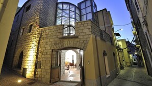 A narrow street with a stone building featuring a large arched entrance and a glass window. - Hotel Antica Posada (Loceri)