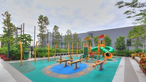 An outdoor playground with various play equipment, surrounded by greenery and a building in the background. - Cybersquare B2210 (Cyberjaya)