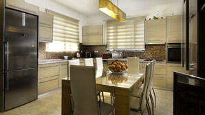 A modern kitchen with a central island, stainless steel appliances, and a dining area with chairs and a table. - Antigone Estate (Rhodes)