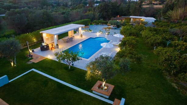 A large swimming pool with a covered patio area, surrounded by well-maintained lawns and trees. - Antigone Estate (Rhodes)