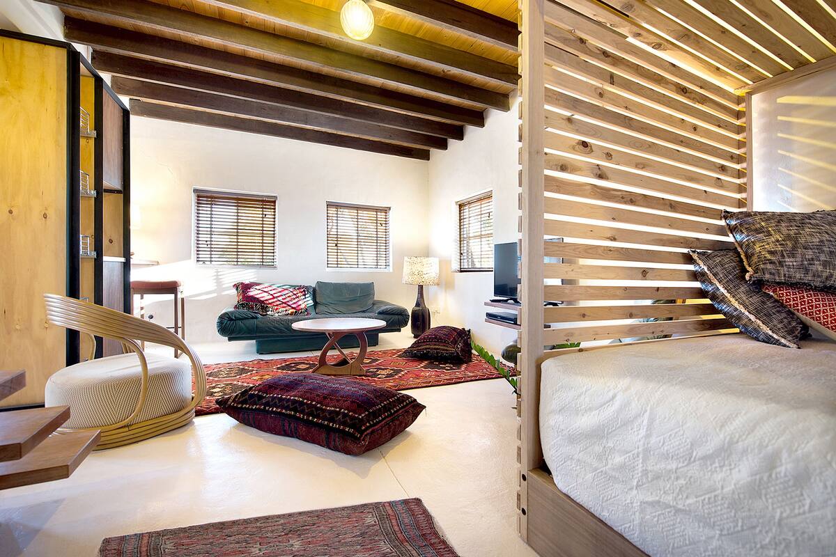 A modern living room with a sofa, a curved chair, a small round table, and a bed with wooden slats.