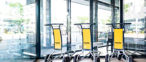 A modern hotel entrance with glass doors and windows, featuring three luggage carts with 'Staycity' branding.