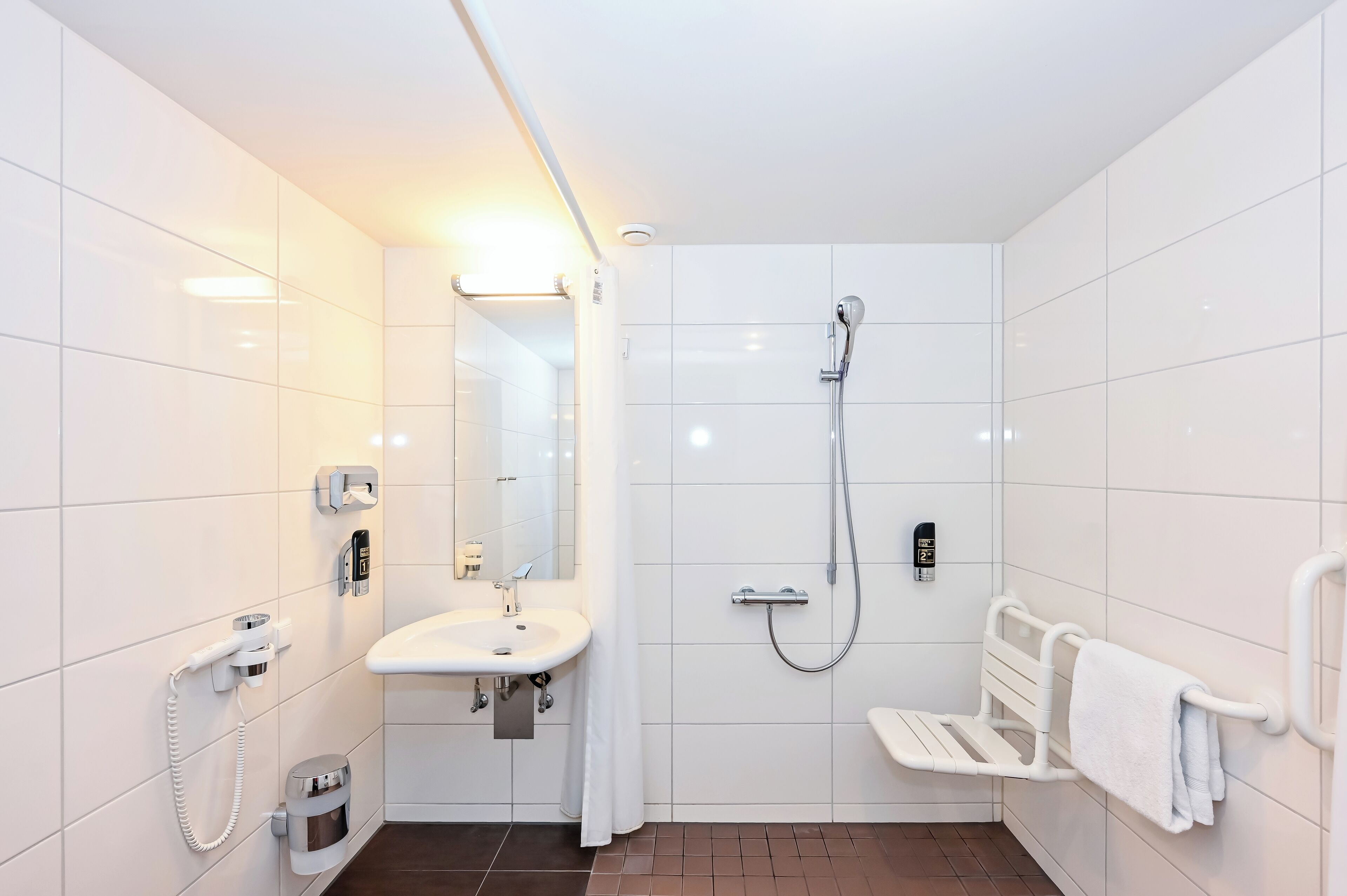 Een moderne badkamer met witte tegels, een wastafel, een douche en een bankje.