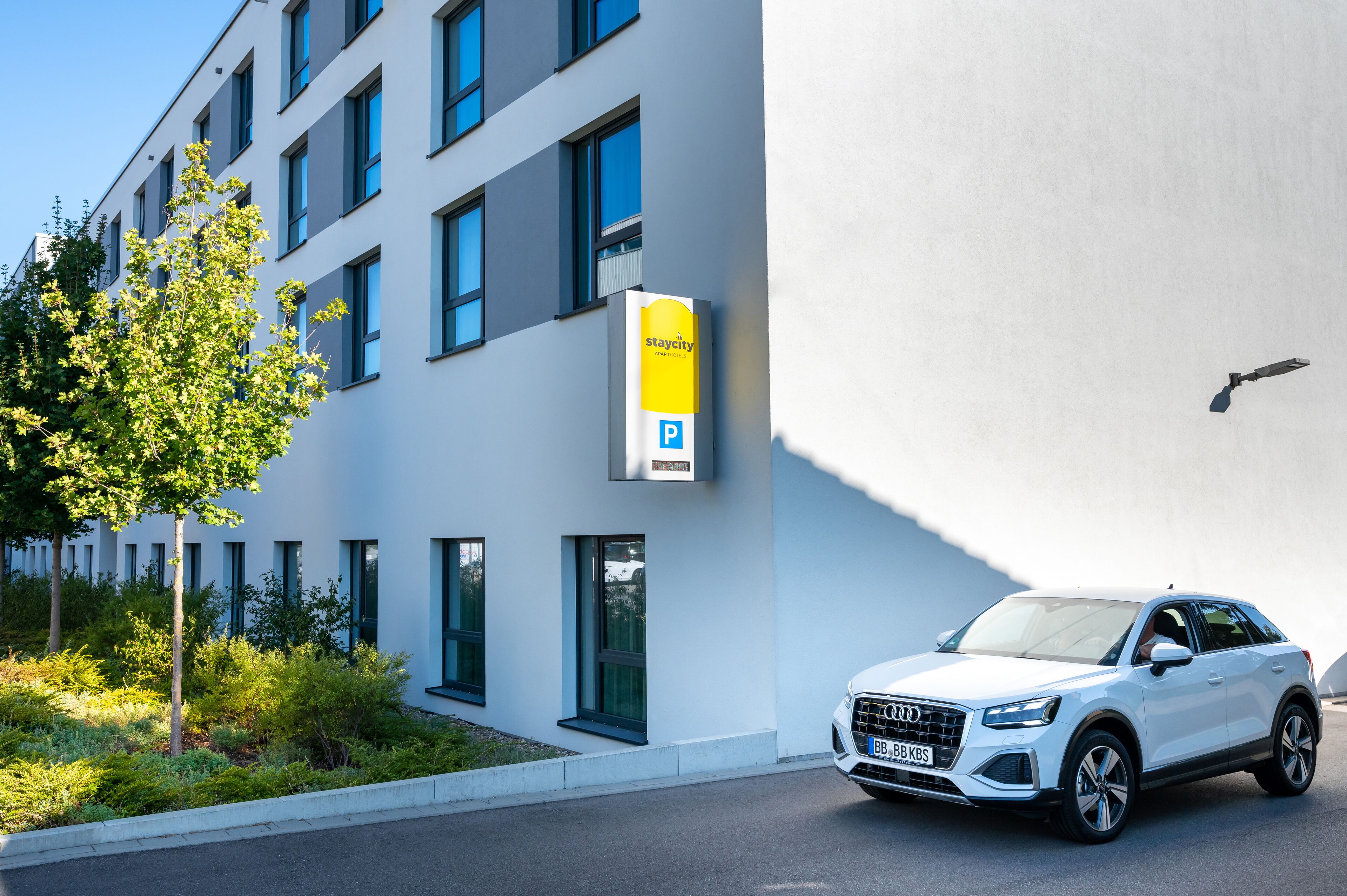 A white Audi SUV parked in front of a modern building with a 'Staycity' parking sign.