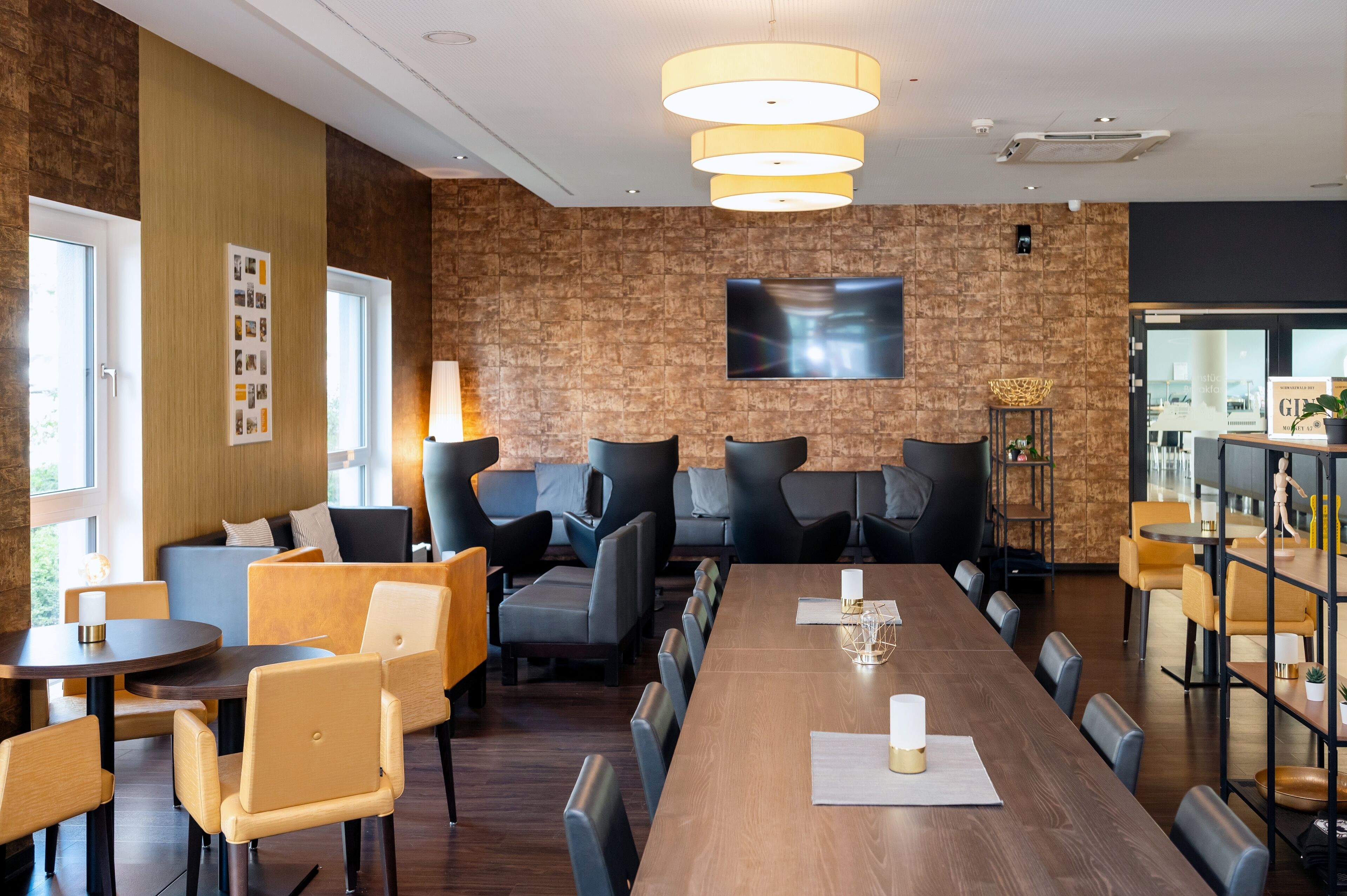 A modern conference room with a long table, comfortable seating, and a large TV screen on the wall.