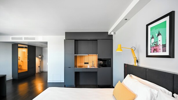 Een moderne hotelkamer met een groot bed, een ingebouwd bureau en een kleine kitchenette.