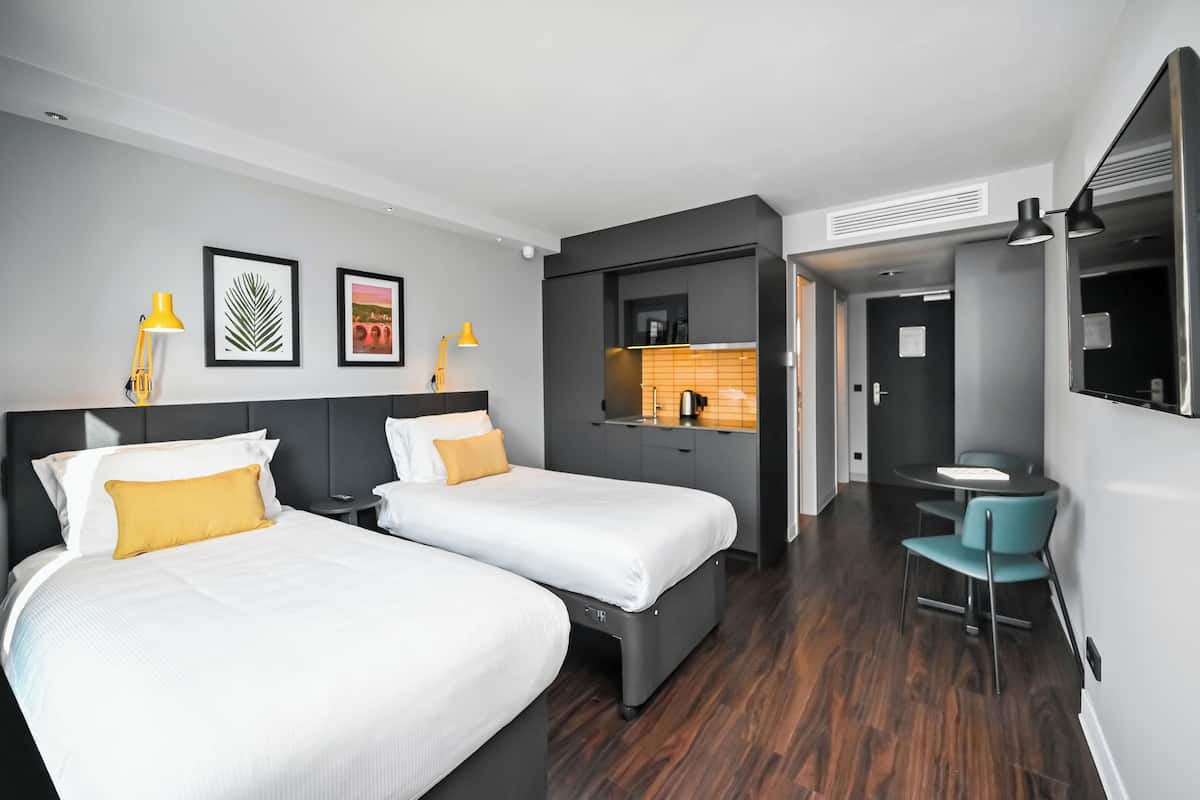 Une chambre d’hôtel avec deux lits, une petite kitchenette, un coin repas et un téléviseur.