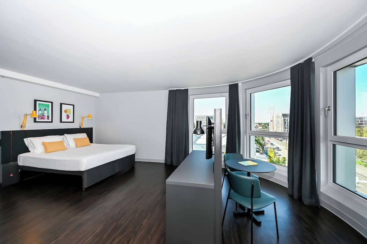 Une chambre d’hôtel moderne, équipée d’un lit, d’un bureau et offrant une vue sur la ville.