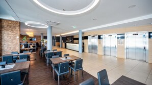 Een moderne hotellobby met een centraal receptiebalie, een zithoek en een rij liften.