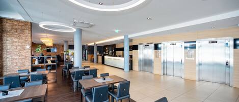 Un moderno vestíbulo de hotel con una recepción central, zona de estar y una fila de ascensores.