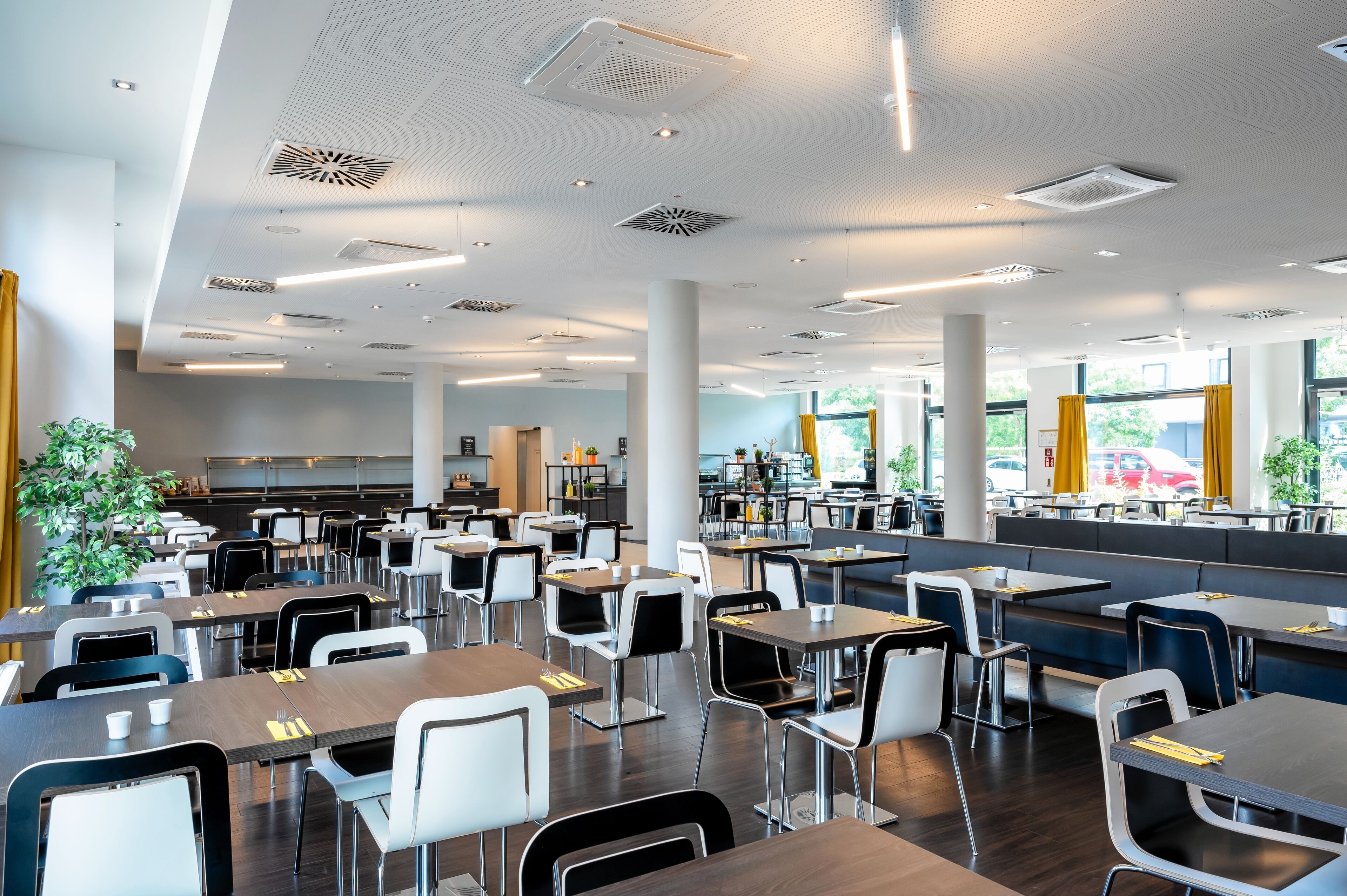 Una amplia cafetería con numerosas mesas y sillas, ventanas grandes y un diseño moderno de techo.