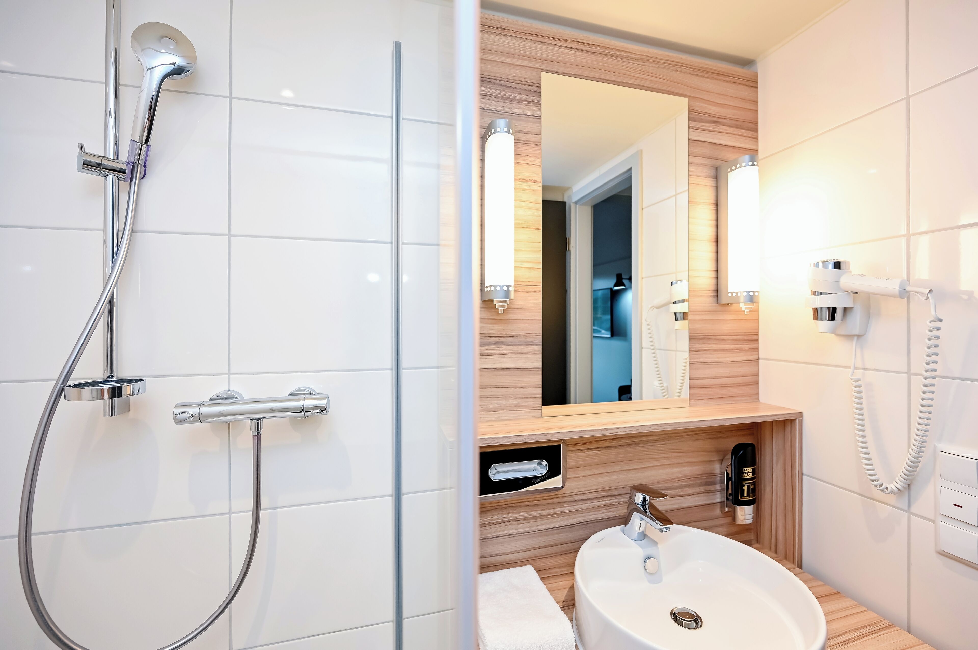 A modern bathroom with a glass-enclosed shower, a wooden vanity, a large mirror, and a white sink.