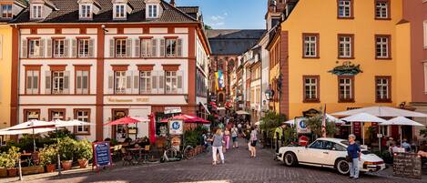 Eine Kopfsteinpflasterstraße mit historischen Gebäuden, Außenbestuhlung und einem Oldtimer.