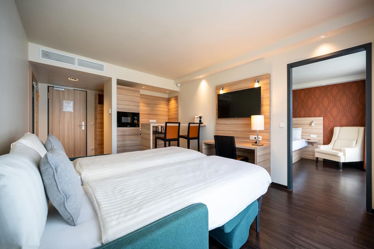 Une chambre d’hôtel avec un grand lit, un bureau, une chaise, une télévision et une salle de bain visible à travers une porte ouverte.