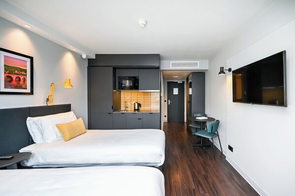 Una habitación de hotel moderna con una cama, una mesita de noche y una pequeña cocina.