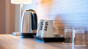 Une chambre d’hôtel équipée d’une machine à café, de deux tasses sur lesquelles est inscrit le mot « séjour », et de deux verres disposés sur un plateau.
