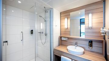Een moderne badkamer met een douchecabine van glas, een houten wastafelmeubel met een wastafel en een spiegel met ingebouwde verlichting.