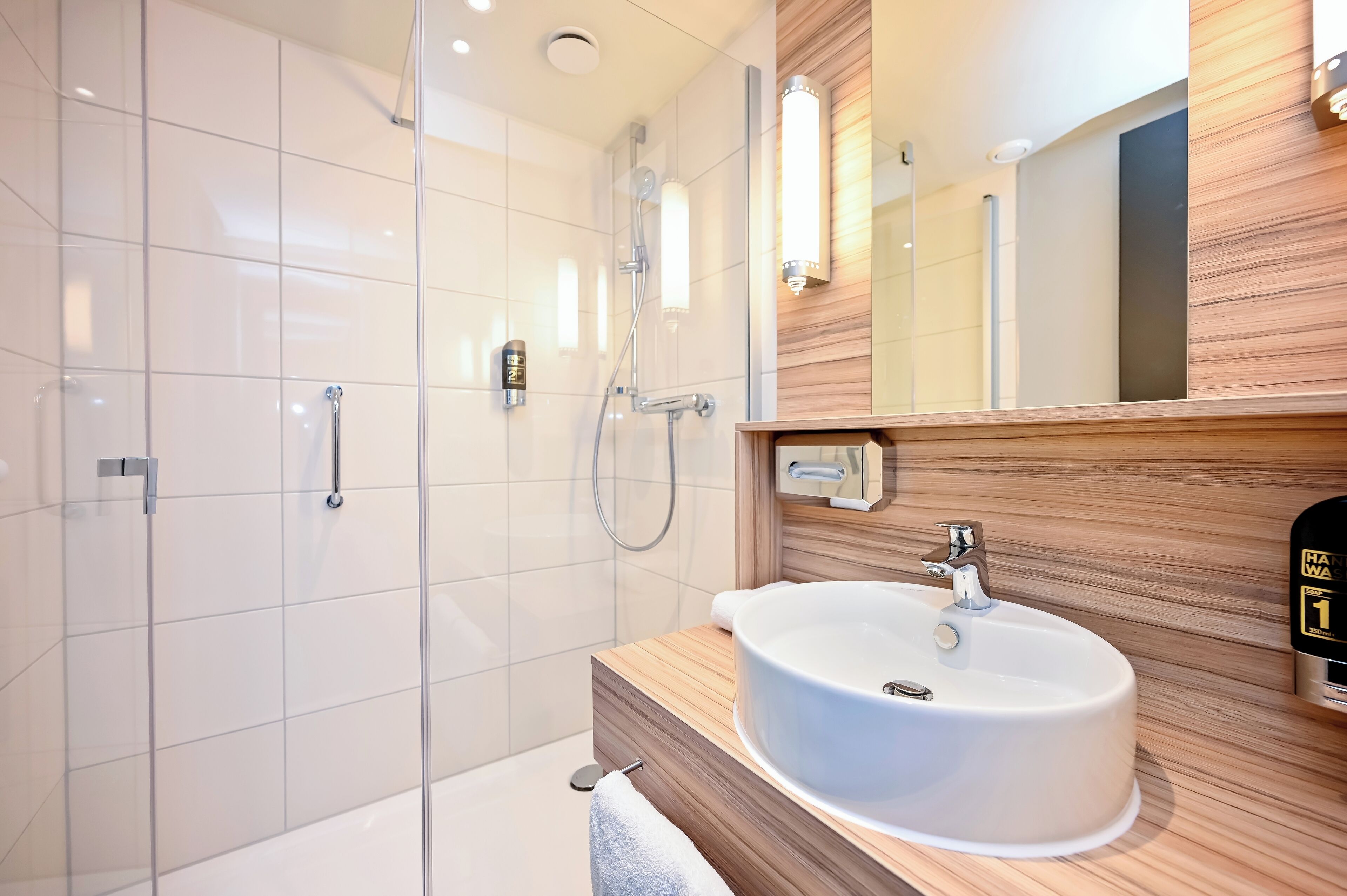 A modern bathroom with a glass shower enclosure, a wooden vanity with a sink, and a mirror with a wooden panel design.