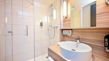 A modern bathroom with a glass shower enclosure, a wooden vanity with a sink, and a mirror with a wooden panel design.