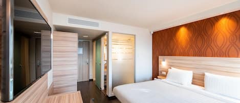 A modern hotel room with a large bed, a flat-screen TV, and a wardrobe.