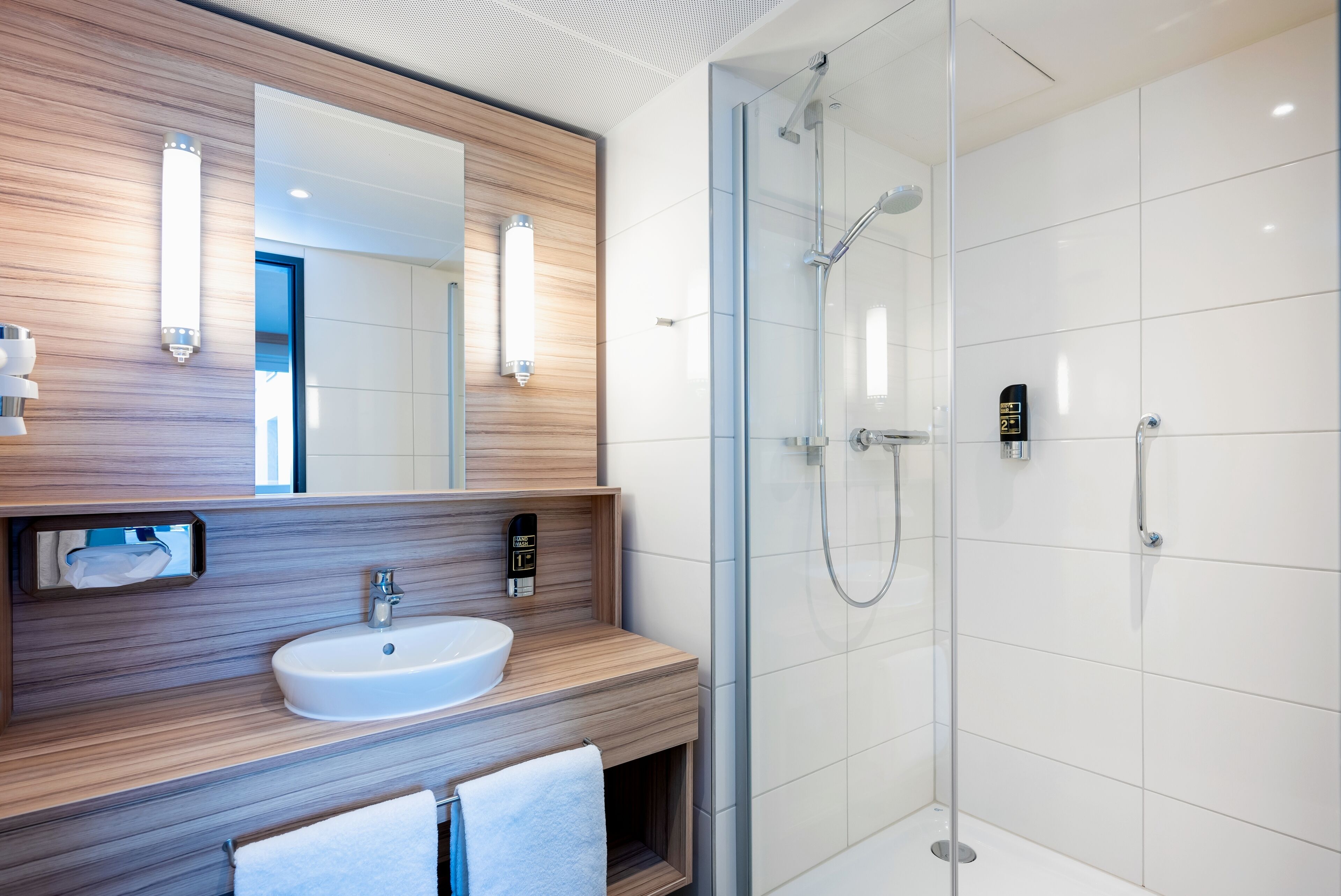 A modern bathroom with a wooden vanity, a white sink, a mirror, and a glass-enclosed shower area.