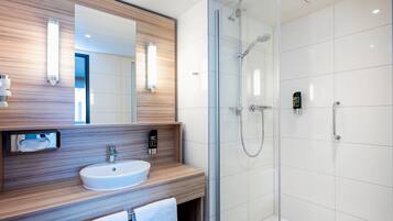 A modern bathroom with a wooden vanity, a white sink, a mirror, and a glass-enclosed shower area.