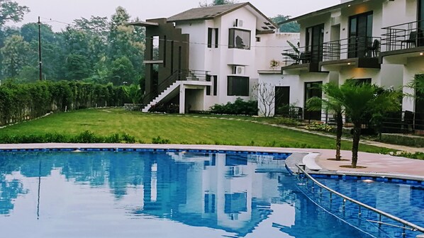 A modern building with a swimming pool, a well-maintained lawn, and a staircase leading to a balcony.