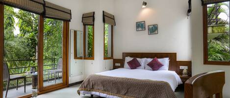 A bedroom with a large bed, a nightstand, a chair, a glass table with a vase and bottles, and a balcony with a chair and table.