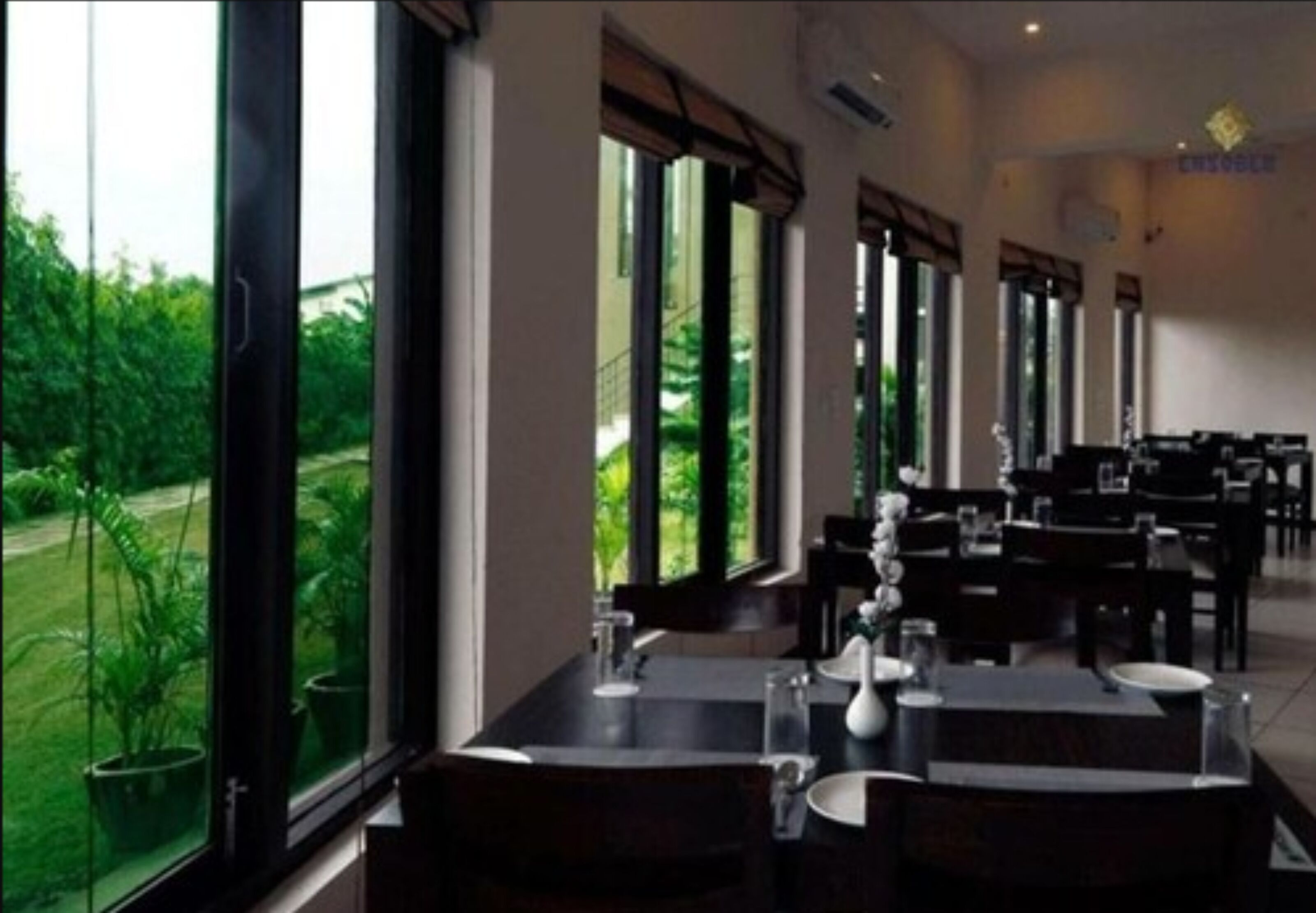 Restaurante com grandes janelas que oferecem vista para o verde. Mesas montadas com louças brancas.