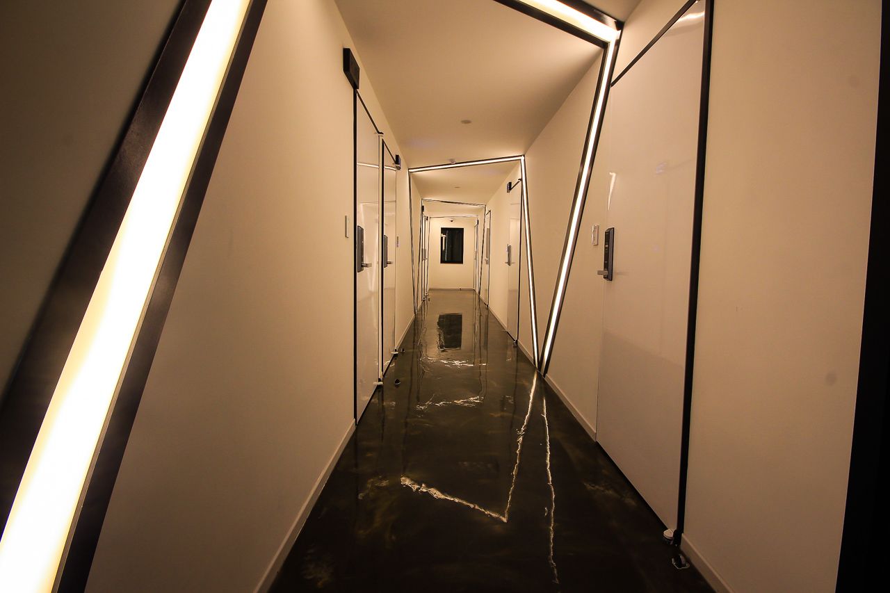 A long, narrow hallway with reflective black flooring and white walls, leading to a door at the end.