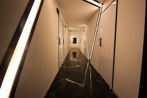 A long, narrow hallway with reflective black flooring and white walls, leading to a door at the end. - Kanu Hotel (Jeonju)