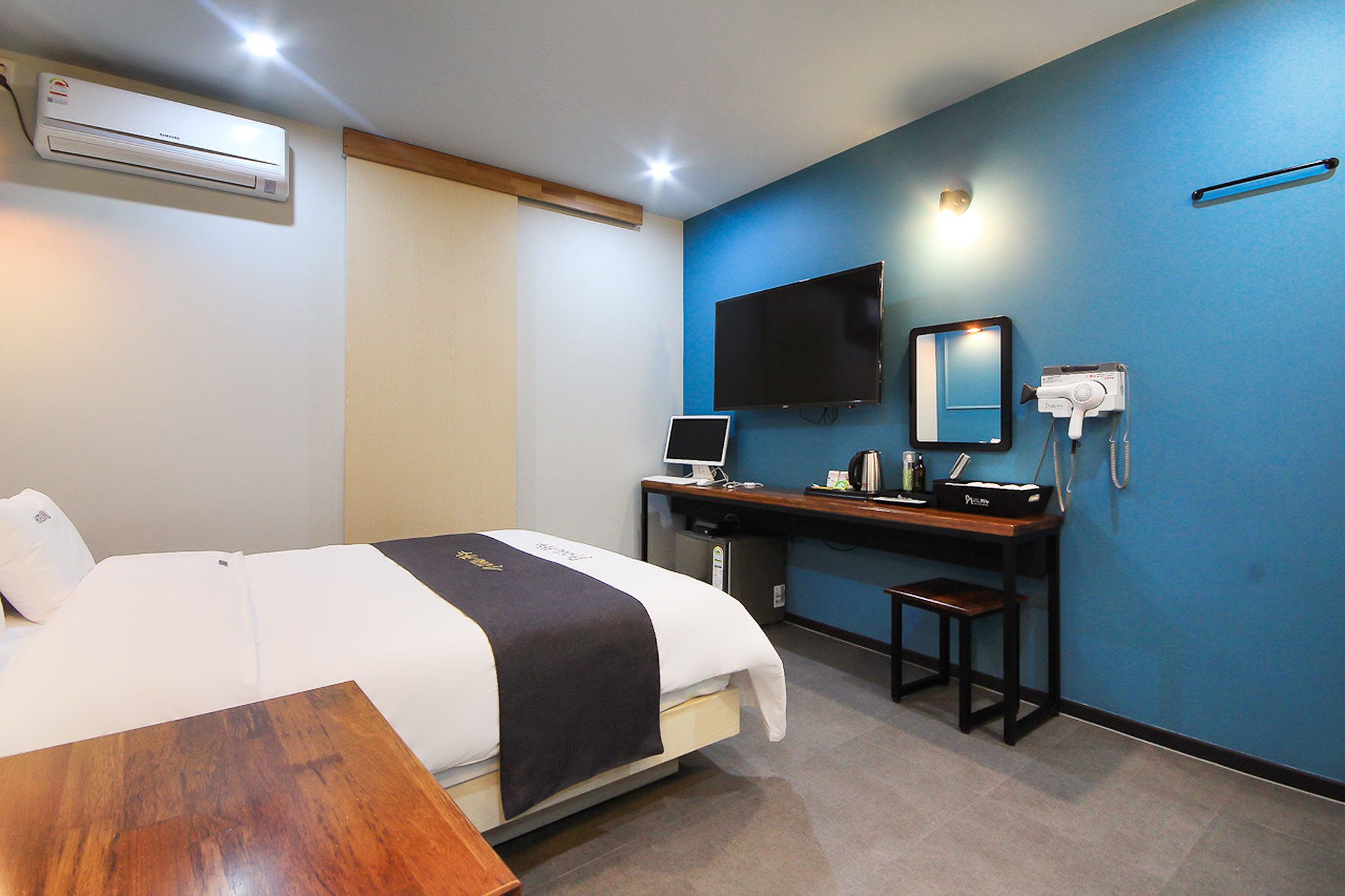 A hotel room with a bed, desk, TV, and air conditioning unit.