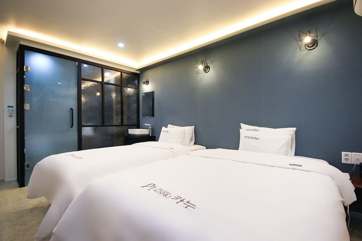 Habitación de hotel con dos camas, un ventanal amplio, un lavamanos y un espejo.