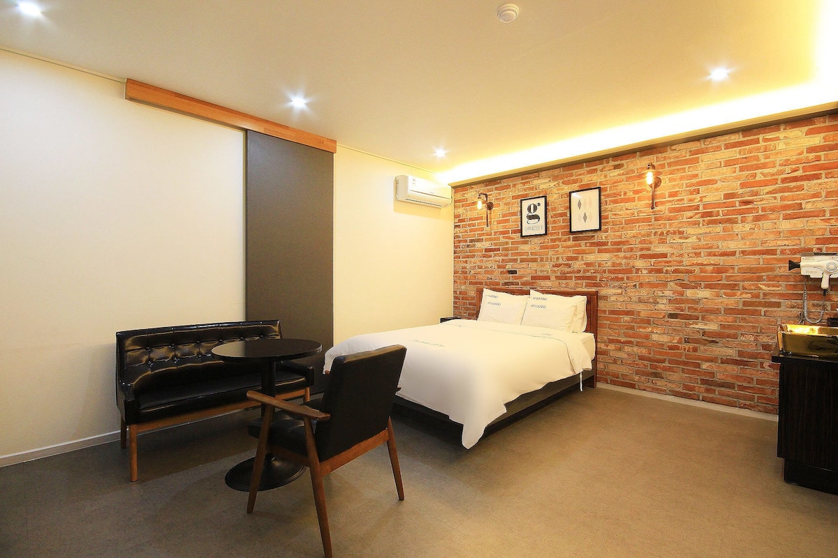 Habitación de hotel con cama, escritorio, silla y pared de ladrillo.