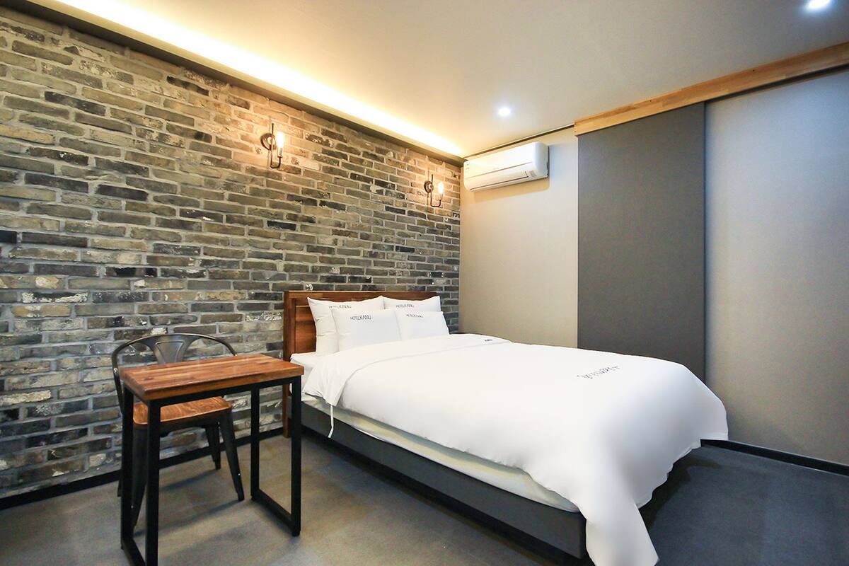 Un dormitorio con pared de ladrillo, estructura de cama de madera, mesita de noche y equipo de aire acondicionado.