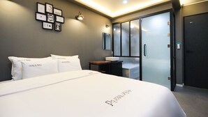 A modern hotel room with a large bed, a bedside table with a sink, and a glass-enclosed shower area. - Kanu Hotel (Jeonju)