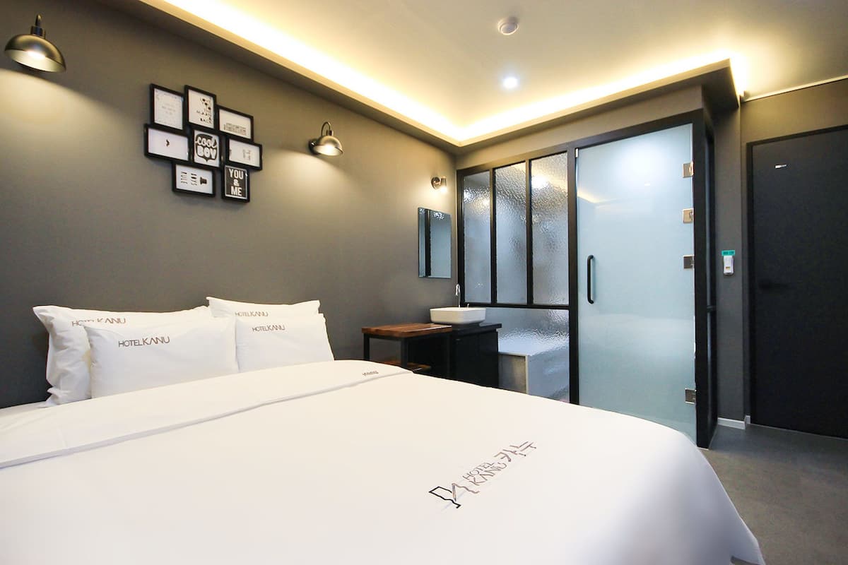 Una habitación de hotel moderna con una cama grande, una mesita de noche con lavamanos y una zona de ducha con paredes de vidrio.