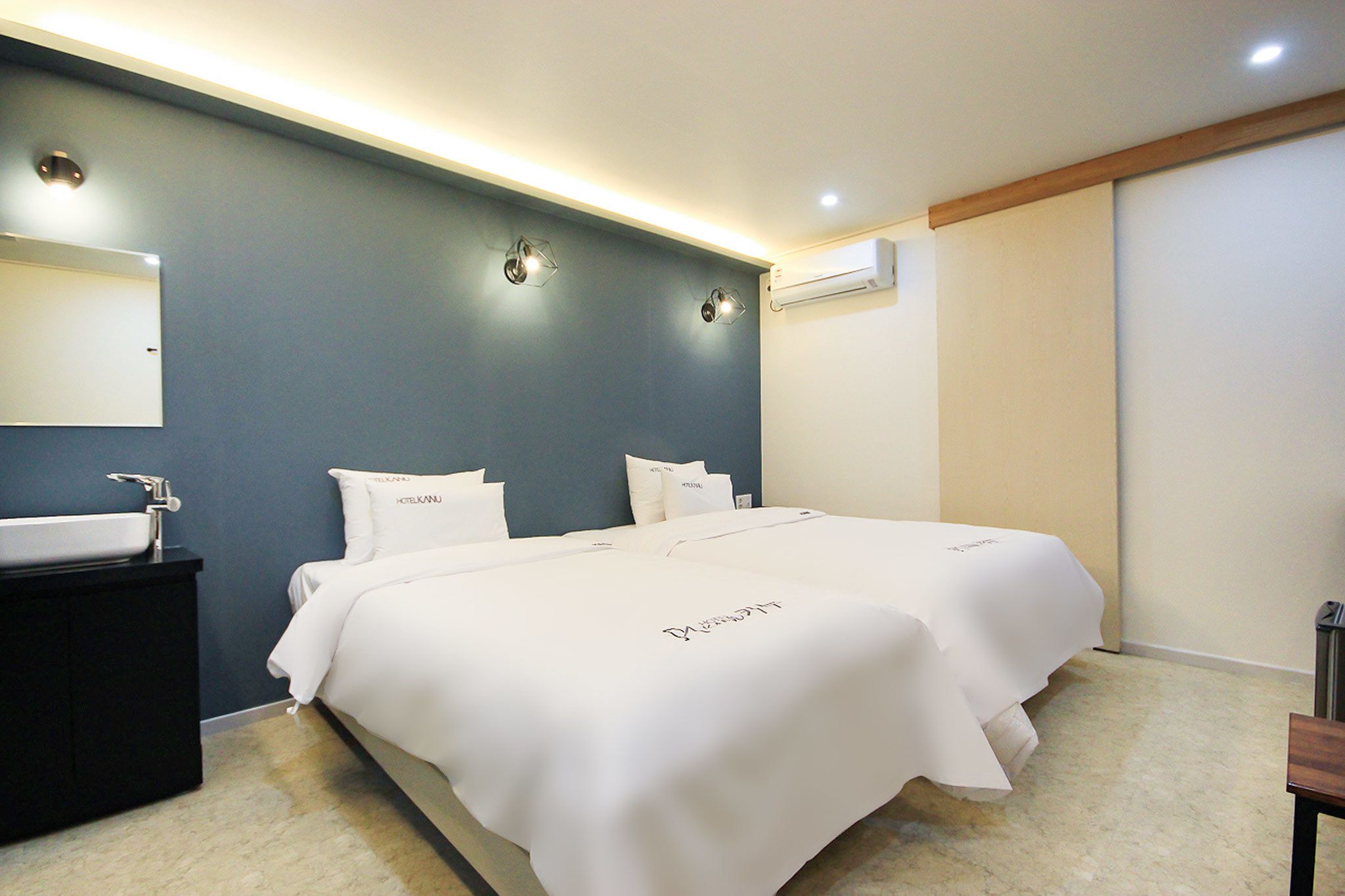 Een moderne hotelkamer met twee bedden, een grote spiegel, een donkere kaptafel en een airconditioner.